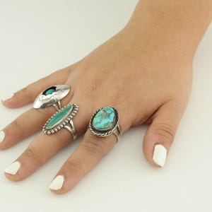May include: Three silver rings with turquoise stones. The rings are on a finger.