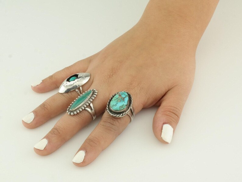 May include: Three silver rings with turquoise stones. The rings are on a finger.