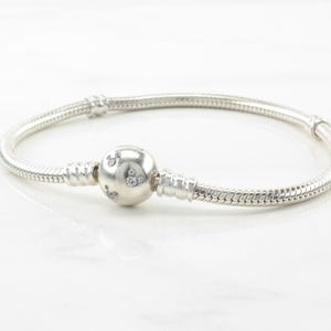 A silver bracelet with a round charm and a snake-shaped clasp.