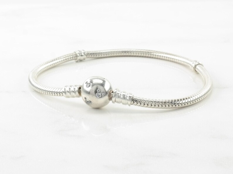 A silver bracelet with a round charm and a snake-shaped clasp.
