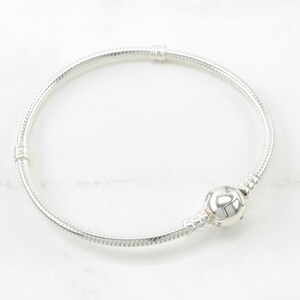 A silver bracelet with a round bead on it, resting on a white marble surface.