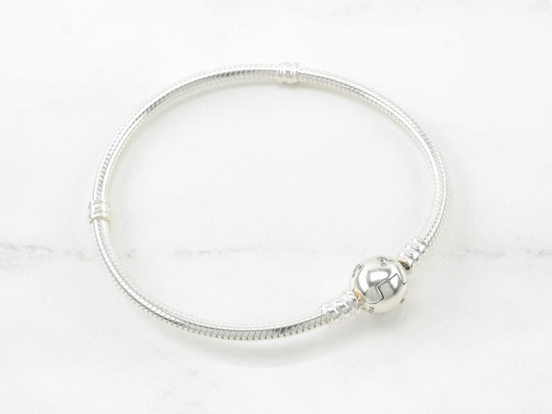 A silver bracelet with a round bead on it, resting on a white marble surface.