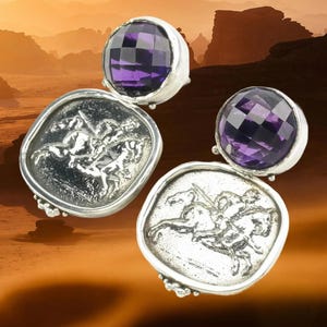 May include: A pair of silver earrings. One earring features a faceted, round, purple gemstone. The other earring has a silver, square-shaped design with a relief of a person on a horse. The background is a desert landscape.