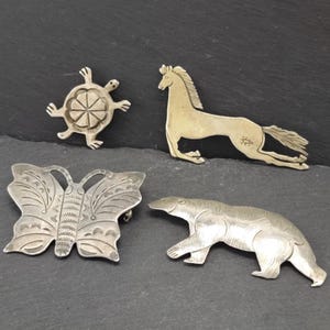 May include: Four silver animal brooches: a turtle, a horse, a butterfly, and a bear. The brooches are all detailed and have a vintage look.
