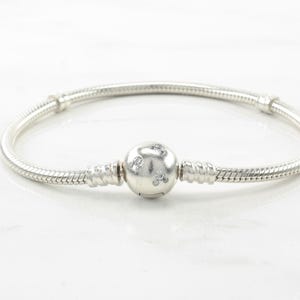 A silver bracelet with a round charm in the center.