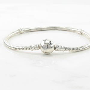 A silver bracelet with a round charm in the center, resting on a white marble surface.