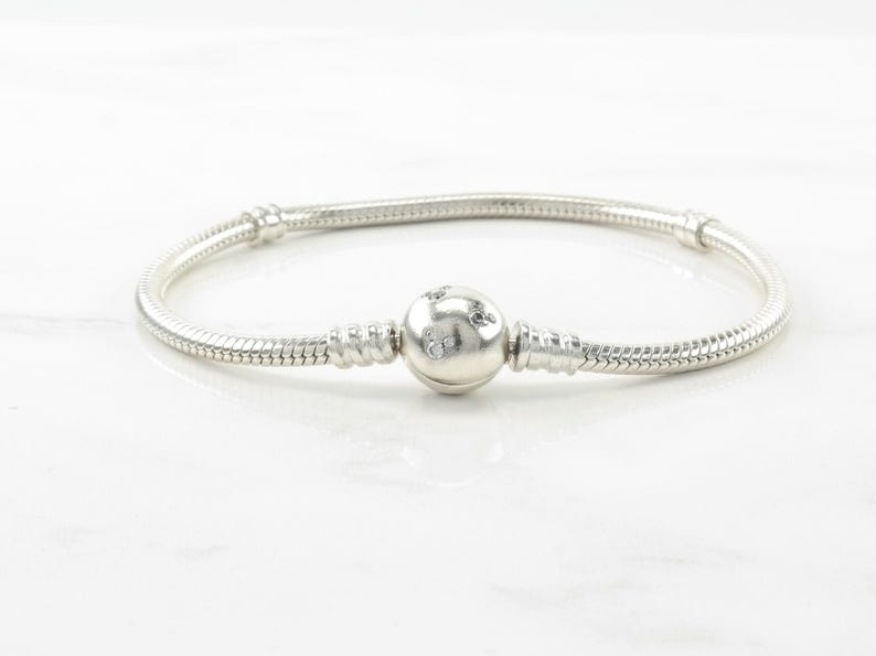 A silver bracelet with a round charm in the center, resting on a white marble surface.