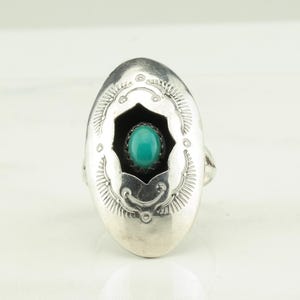 May include: A silver ring with an oval shaped setting. The setting has a turquoise stone in the center and a black background. The ring is decorated with a silver design around the edge.