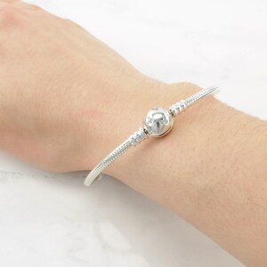 A silver bracelet with a round charm is worn on a person's wrist.