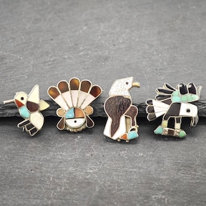 Puede incluir: Cuatro alfileres de estilo nativo americano con un colibrí, un tocado, un águila y un pájaro con un diseño en blanco y negro. Los alfileres están hechos de plata e incrustados con turquesa, coral y otras piedras.