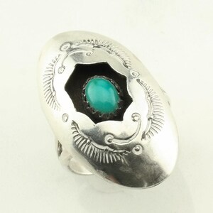 May include: A silver ring with a turquoise stone set in a starburst design. The ring is oval shaped and has a detailed design around the stone.
