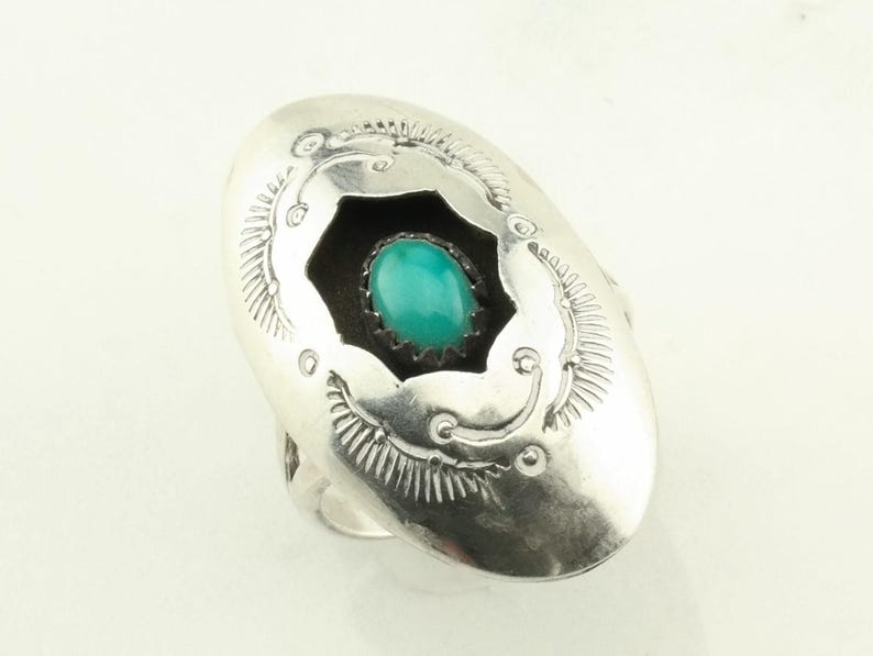 May include: A silver ring with a turquoise stone set in a starburst design. The ring is oval shaped and has a detailed design around the stone.
