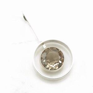 Peut inclure: Un pendentif en argent avec une pierre pr&eacute;cieuse ronde et facet&eacute;e de couleur brun clair sertie dans un cercle.