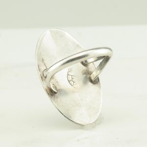 May include: A silver ring with an oval shaped stone. The back of the ring has a stamped design.