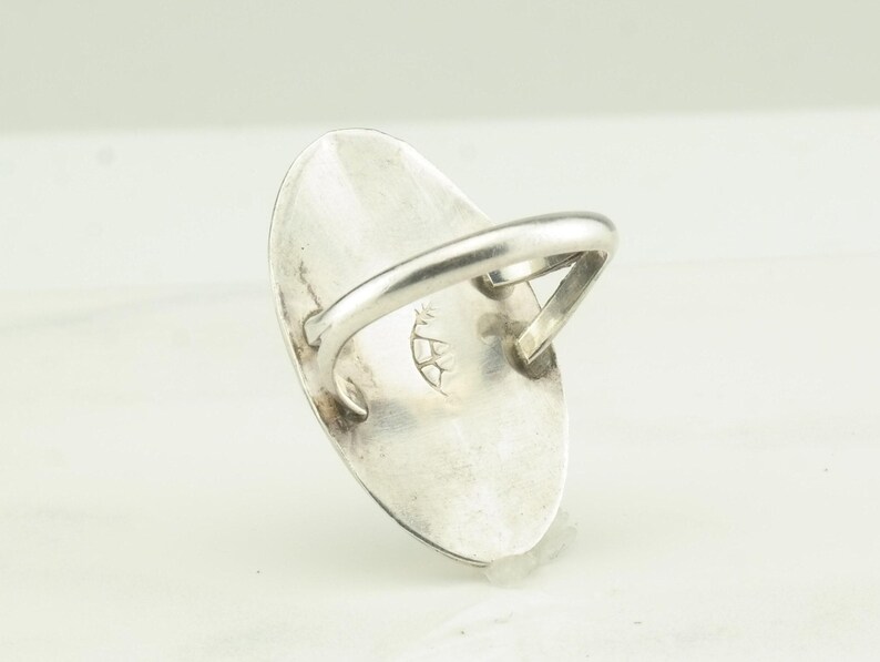 May include: A silver ring with an oval shaped stone. The back of the ring has a stamped design.
