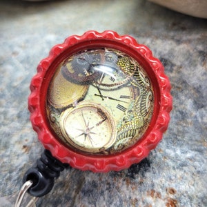 May include: A red retractable badge holder with a round, clear, glass-like top featuring a vintage clock face design.