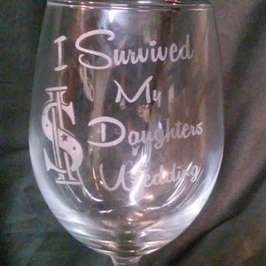 May include: A clear glass wine glass with the text "I Survived My Daughters Wedding" etched on the side. The text is in a cursive font and includes a stylized dollar sign.