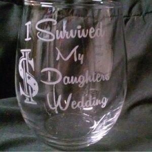 May include: A clear glass wine glass with the text "I Survived My Daughters Wedding" etched on the side. The text is in a white font and includes a dollar sign graphic.