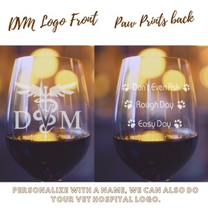 Può includere: Due bicchieri da vino con disegni incisi. Il bicchiere anteriore ha un logo DVM con un serpente e ali. Il bicchiere posteriore ha impronte di zampe e il testo "Don't Even Ask", "Rough Day" e "Easy Day".