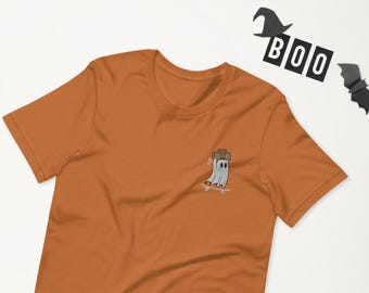 May include: A burnt orange t-shirt with a white ghost wearing a boombox and skateboarding. The ghost is embroidered on the shirt.