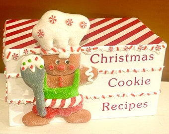 Könnte beinhalten: Eine Weihnachtsplätzchen-Rezeptbox mit einem Lebkuchen-Koch mit weißer Kochmütze und grüner Schürze. Die Box ist weiß mit rot-weiß gestreiften Akzenten und den Worten "Christmas Cookie Recipes".