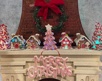 Può includere: Un camino in mattoni bianchi decorato con un villaggio di Natale a tema bastoncino di zucchero rosso e verde. Il villaggio comprende un albero di Natale a bastoncino di zucchero, case di pan di zenzero e un cartello che dice "Buon Natale".