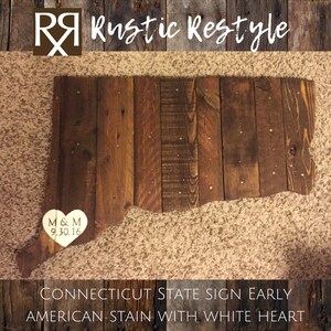 May include: Wooden sign shaped like the state of Connecticut, stained in a dark brown color with a white heart in the lower left corner. The heart has the initials "M & M" and the date "9.30.16" inscribed on it. The sign reads "CONNECTICUT STATE SIGN EARLY AMERICAN STAIN WITH WHITE HEART".