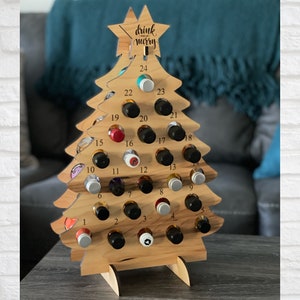 May include: Wooden Christmas tree advent calendar with 24 numbered slots for small bottles. The tree is decorated with the text "drink and be merry".