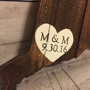 May include: A wooden sign with a white heart painted on it. The heart has the initials "M & M" and the date "9.30.16" written in black.