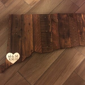 May include: A wooden outline of the state of Connecticut with a gold heart attached to the bottom. The heart has the initials "M & M" and the date "9.30.16" engraved on it.