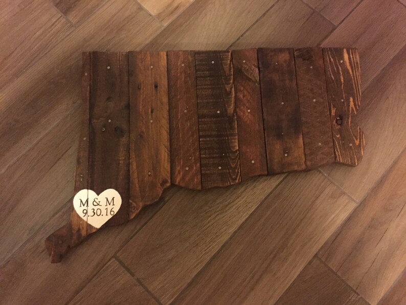 May include: A wooden outline of the state of Connecticut with a gold heart attached to the bottom. The heart has the initials "M & M" and the date "9.30.16" engraved on it.