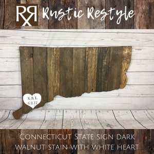 May include: A wooden state sign of Connecticut in the shape of the state with a white heart in the center. The heart has the initials "K&L" and the date "6.2.17" inside. The sign is stained dark walnut and has a rustic look. The sign is on a white wooden background.  CONNECTICUT STATE SIGN DARK WALNUT STAIN WITH WHITE HEART