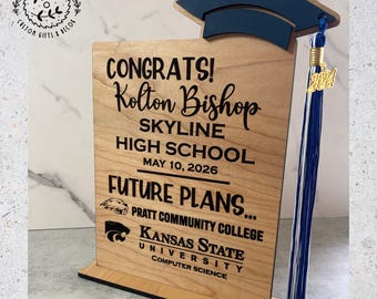 May include: A wooden graduation sign with a navy blue cap and tassel. The sign reads "CONGRATS! Kolton Bishop SKYLINE HIGH SCHOOL MAY 10, 2026 FUTURE PLANS..." with college logos and "2024" on the tassel.
