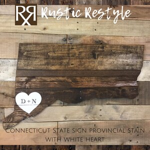 May include: Wooden state of Connecticut sign with a white heart and the initials "D+N" painted on it. The sign is stained in a provincial color.