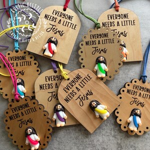 May include: Wooden tags with the phrase "EVERYONE NEEDS A LITTLE Jesus" and a small Jesus figurine. The tags are in various shapes and sizes, with colorful cords for hanging. The figurines have different colored robes.