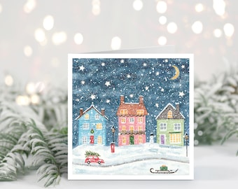May include: A square greeting card featuring a watercolor illustration of a snowy winter village at night. The scene includes a blue house, a pink house, and a green house under a starry sky with a crescent moon. A red car carries a tree.
