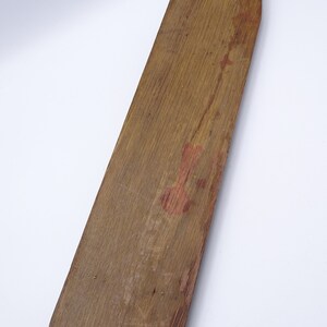 K&ouml;nnte beinhalten: Ein langes, schmales Holzpaddel mit abgerundeter Oberseite und spitzem Boden. Das Paddel ist aus hellbraunem Holz gefertigt und hat ein paar kleine L&ouml;cher, die hineingebohrt wurden. Auf der Oberfl&auml;che befinden sich schwache rote Farbmale.