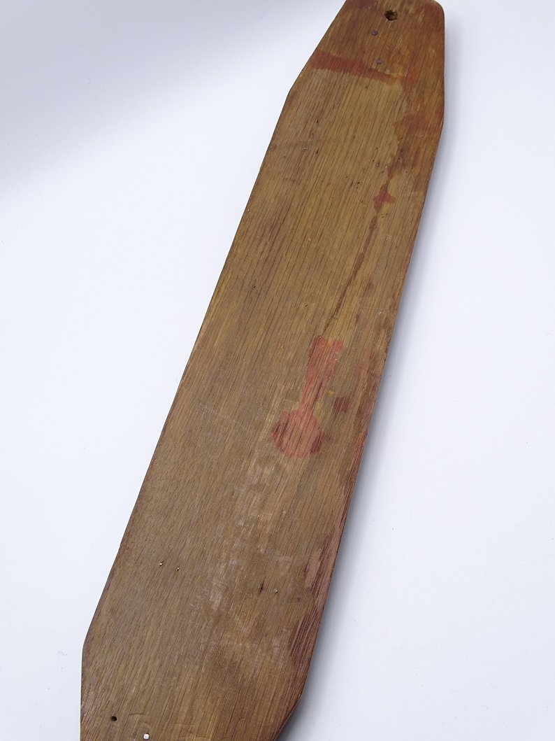 K&ouml;nnte beinhalten: Ein langes, schmales Holzpaddel mit abgerundeter Oberseite und spitzem Boden. Das Paddel ist aus hellbraunem Holz gefertigt und hat ein paar kleine L&ouml;cher, die hineingebohrt wurden. Auf der Oberfl&auml;che befinden sich schwache rote Farbmale.