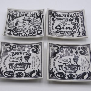 May include: Four square ceramic dishes with black and white vintage-style graphics. The dishes feature text and illustrations, including phrases like "Mellow Yellow Tobacco" and "Betty's Bathtub." The overall theme is retro and humorous.