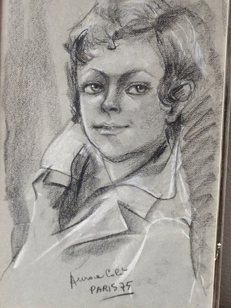 May include: A black and white charcoal drawing of a young person with short hair. The drawing is signed "Aurora Cole PARIS 75".