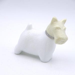 May include: White ceramic dog figurine with a silver collar. The dog is in a standing position with its head tilted to the side. The figurine is a whimsical and decorative piece.