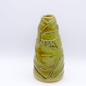 Può includere: Un vaso in ceramica verde con un designo testurizzato e piegato. Il vaso ha una base larga e un'apertura stretta.