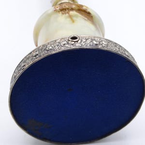 May include: An antique decorative bell with a silver-colored floral patterned rim and a blue base. The bell has a light green and brown marbled body and a chain. The bell is viewed from below.