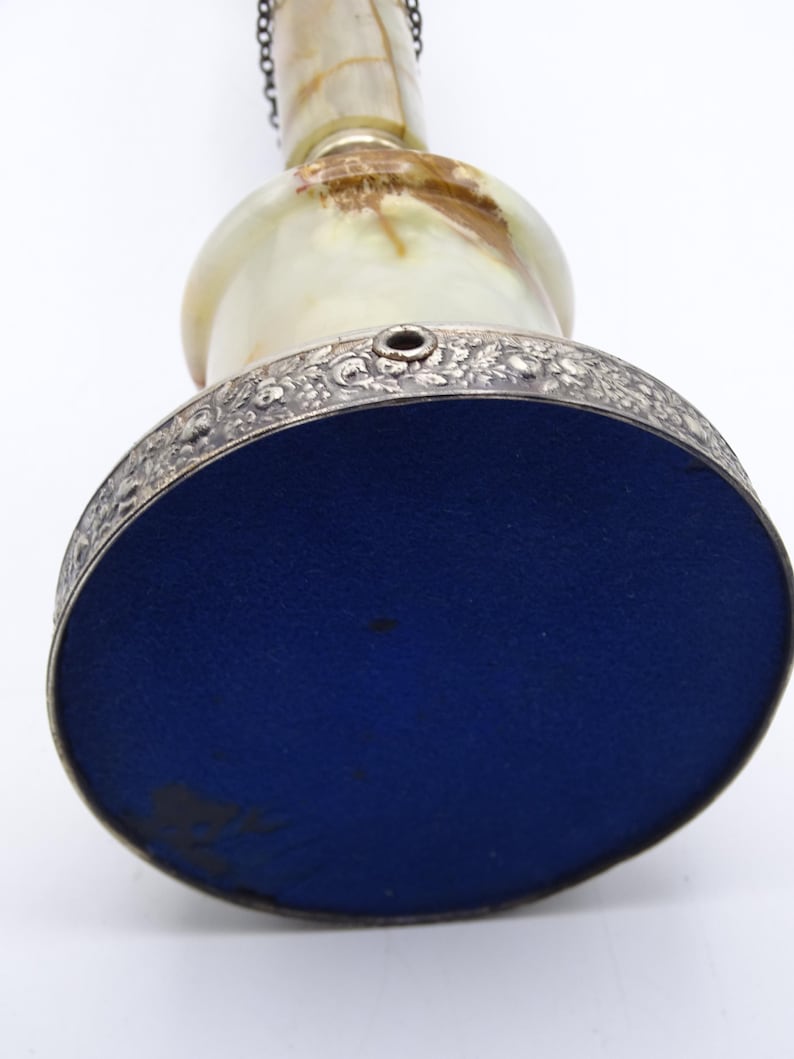 May include: An antique decorative bell with a silver-colored floral patterned rim and a blue base. The bell has a light green and brown marbled body and a chain. The bell is viewed from below.