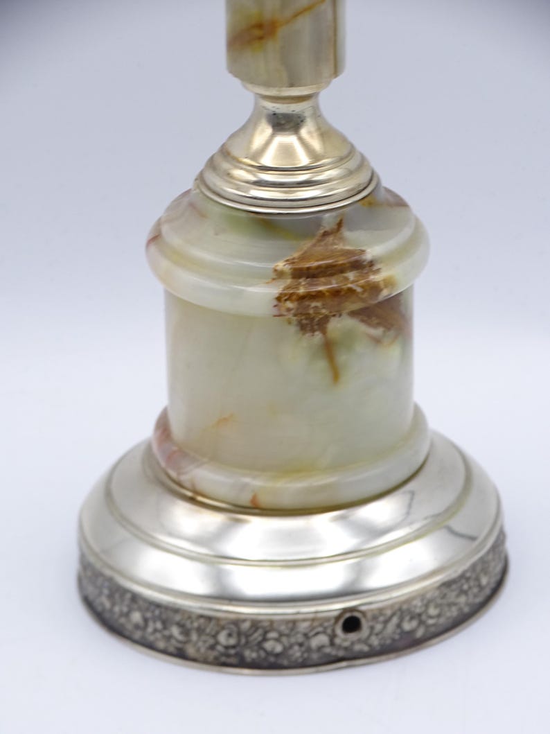 May include: A decorative lamp with a silver base and accents. The lamp's body is made of a light green and brown onyx material. The base has a detailed floral pattern around the bottom edge. The lamp is a unique home decor item.