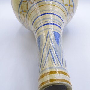 May include: A ceramic vase with a white background and blue and gold geometric patterns. The vase has a wide, round top and a narrow, cylindrical base.