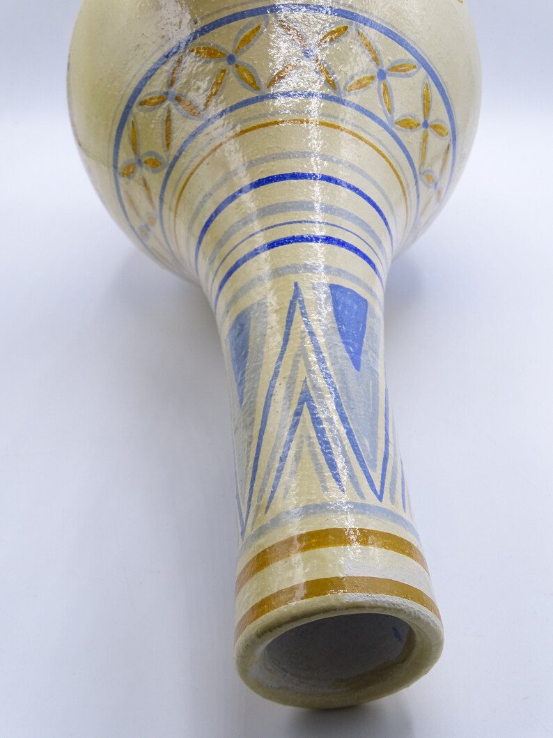 May include: A ceramic vase with a white background and blue and gold geometric patterns. The vase has a wide, round top and a narrow, cylindrical base.