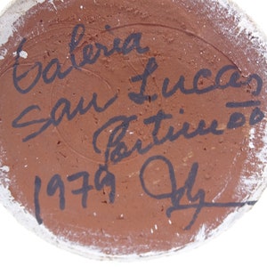 May include: Close-up of the bottom of a ceramic vase with a brown glaze. The vase is signed "Galeria San Lucas" and dated "1979 July".