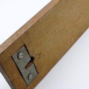 May include: A wooden ruler with a metal bracket and two screws. The ruler is brown and the bracket is silver.