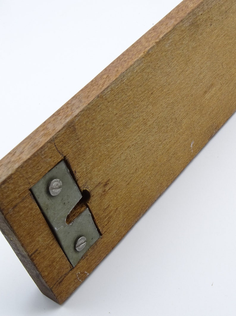 May include: A wooden ruler with a metal bracket and two screws. The ruler is brown and the bracket is silver.